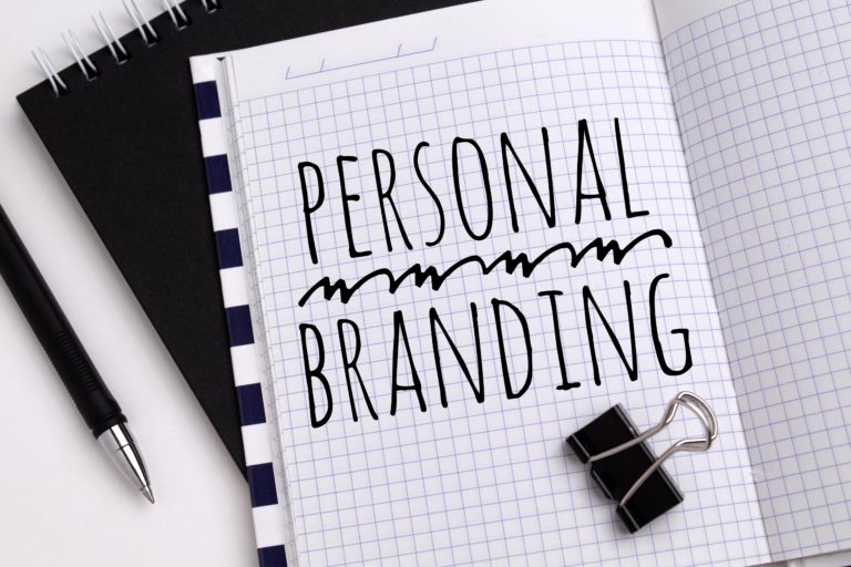 alt="the term personal branding is written on notebook page with a pen and paper clip placed near it"