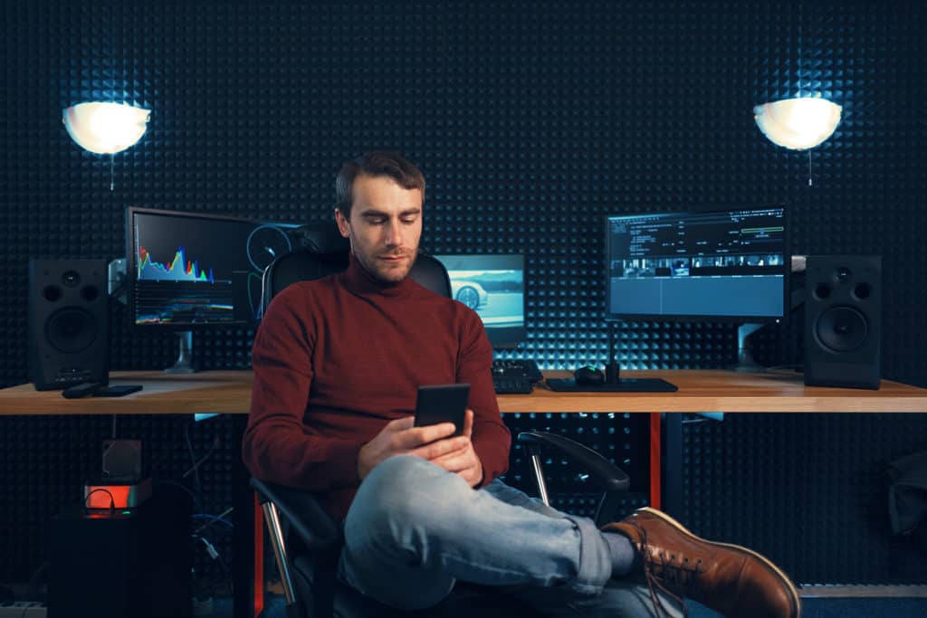 alt="Young man working in the studio using a smartphone and computers"