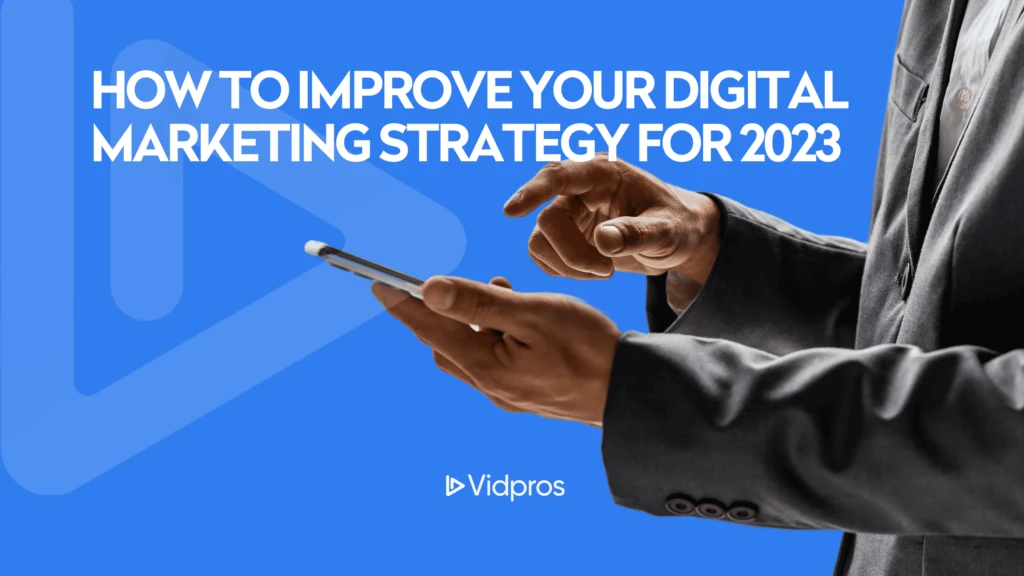 A person in a suit holds a smartphone against a blue background. The text reads, How to improve your digital marketing strategy for 2023. The Vidpros logo is at the bottom.